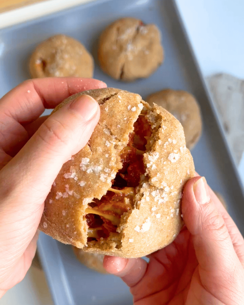 two hands opening a pepperoni pizza bun with melty cheese being pulled a part