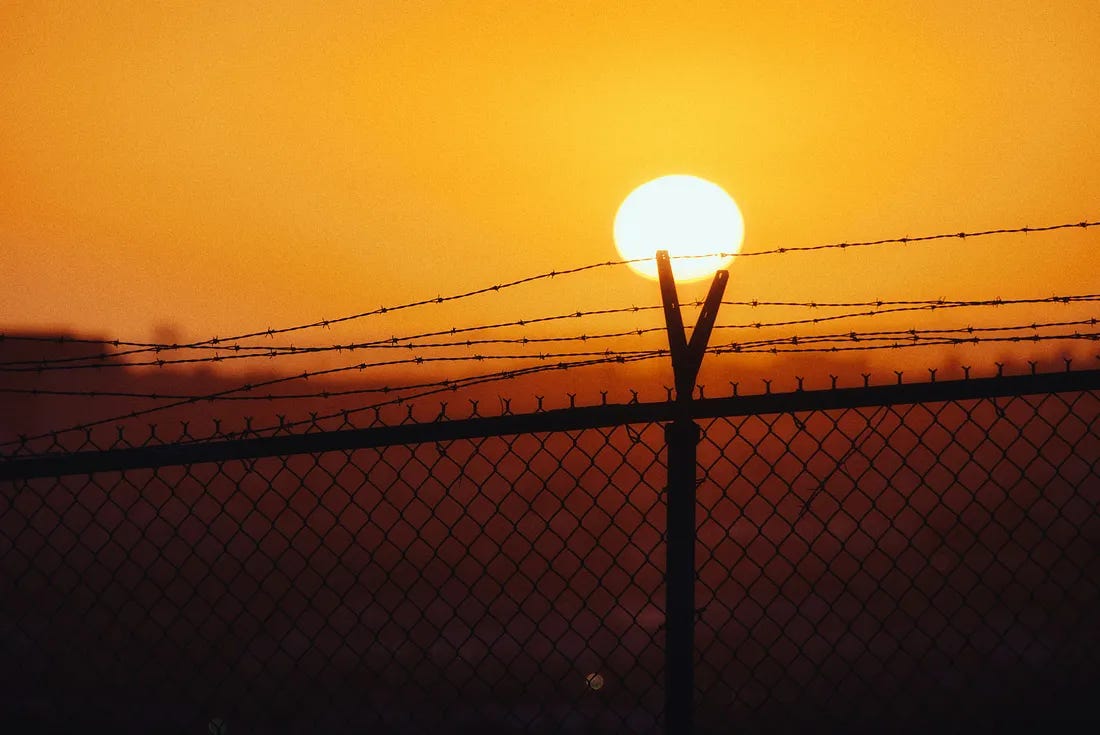 barbwired fence looking out to an orange sunset barbwired fence looking out to an orange sunset