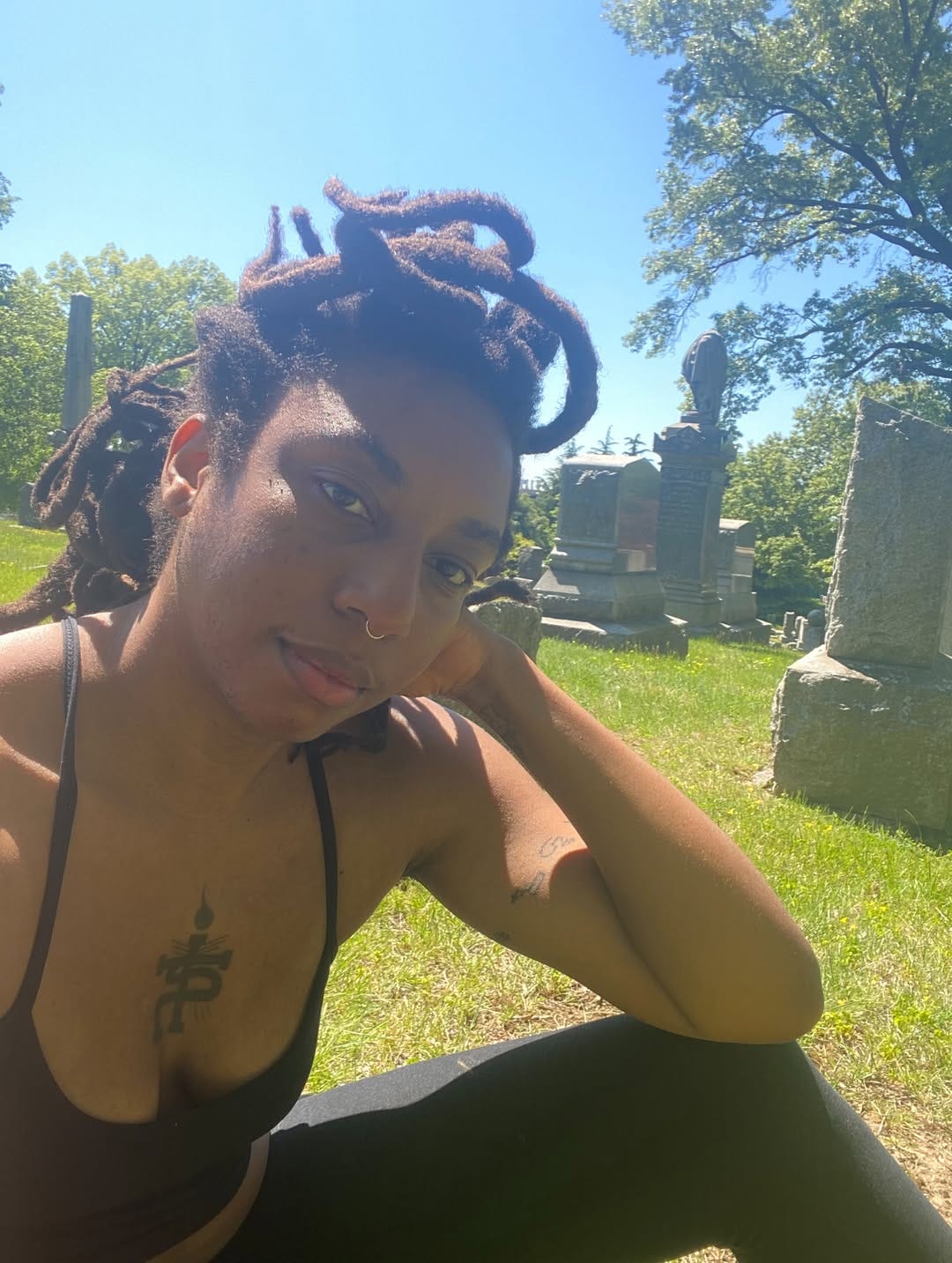 N3VLYNNN sitting alone in an old cemetery on a beautiful spring day. She is smiling into the camera with her head resting in her palm