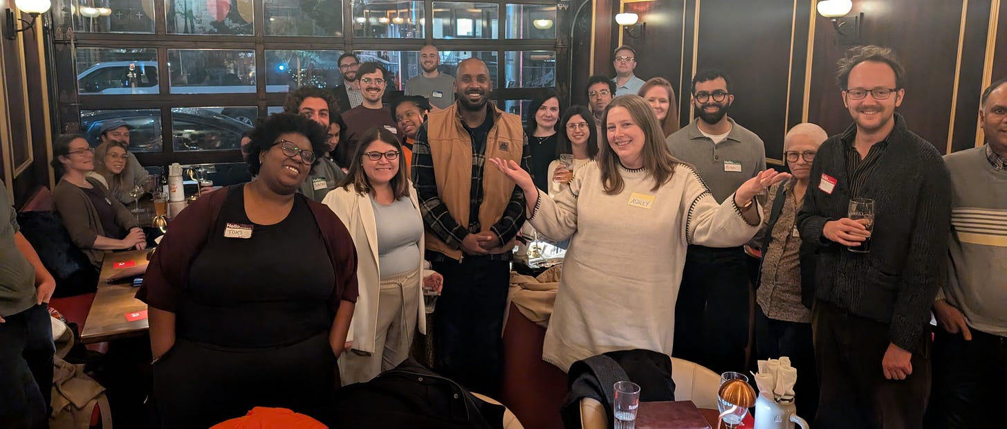 A diverse group of people in a bar smile at the camera.