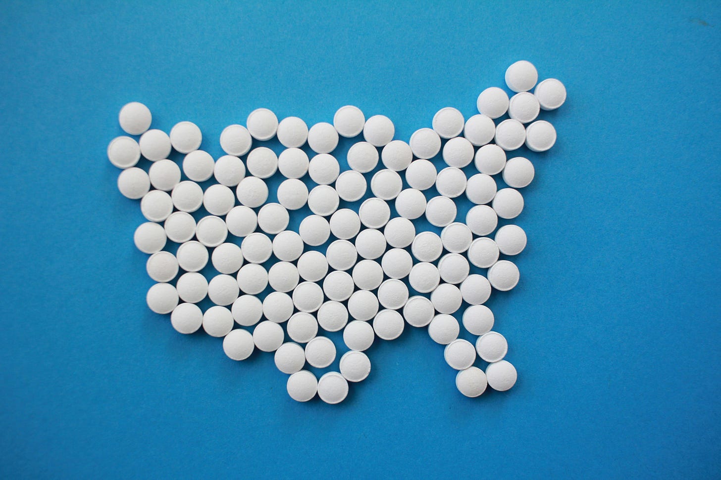 White pills on a blue background arranged to form the rough outline of the USA. Image credit: Hal Gatewood/Unsplash