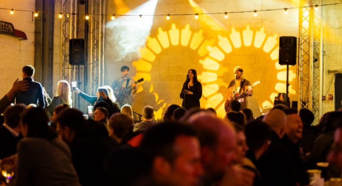 A live band playing on stage at The Garage Chilwell with yellow lights behind them and a crowd in front of them