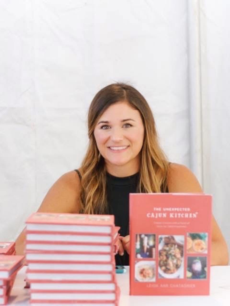Leigh Ann sitting with copies of her book, The Unexpected Cajun Kitchen piled in front of her Leigh Ann sitting with copies of her book, The Unexpected Cajun Kitchen piled in front of her