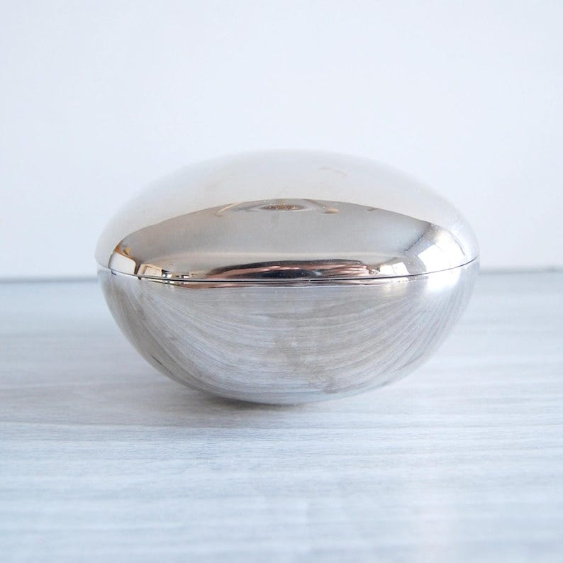 May include: A silver, egg-shaped trinket box with a smooth, reflective surface.