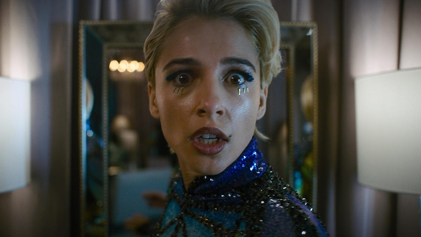 Naomi Scott in crazy popstar makeup looking at the camera in horror.
