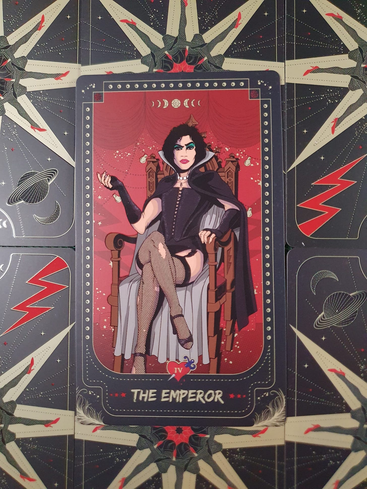 The Emperor card from a theatrical-themed tarot deck, depicting a dark-haired figure in dramatic makeup, black corset, fishnet stockings and a cape, seated confidently on an ornate throne. The Emperor card from a theatrical-themed tarot deck, depicting a dark-haired figure in dramatic makeup, black corset, fishnet stockings and a cape, seated confidently on an ornate throne.