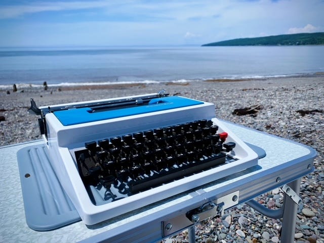A dark-haired woman sits with a typewriter in a botanical garden, a freshly typed poem sits on a blue vintage trypewriter, a typewriter sits on a table on a rocky beach, a pink lotus flower blossoms in a lily pond