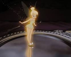A classic animated still from the 1953 Disney movie Peter Pan, featuring Tinker Bell. The character is shown in a close-up, surrounded by glowing, shimmering golden pixie dust that reflects off her wings and creates a magical, luminous aura.