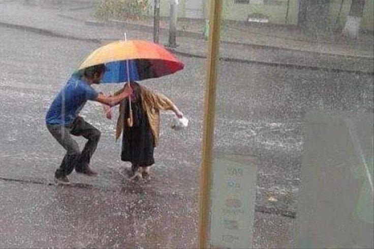 This may contain: a man and woman holding an umbrella in the rain on a city street as it rains