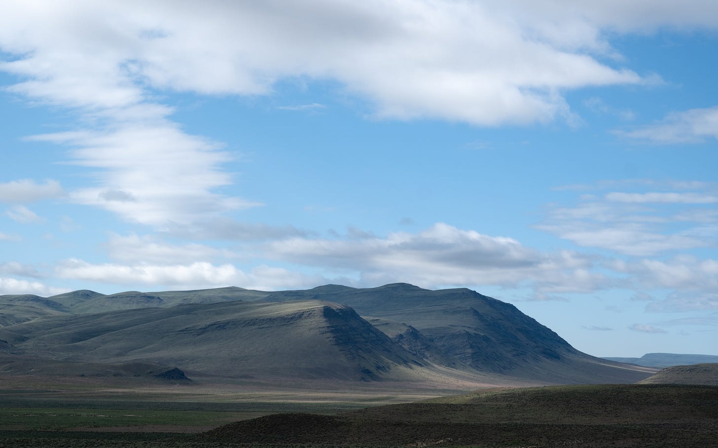 A stark low mountain range is set off against blue skies and white cloiuds, no civilization in sight.
