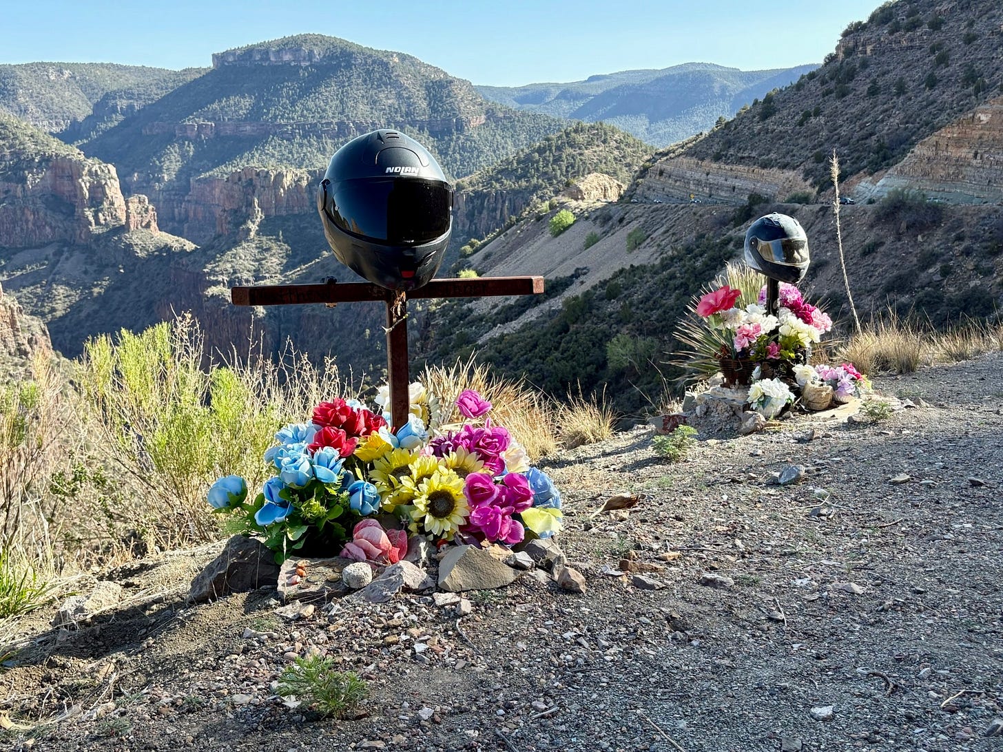two black motorcycle helmets atop crosses with flowers at the ground
