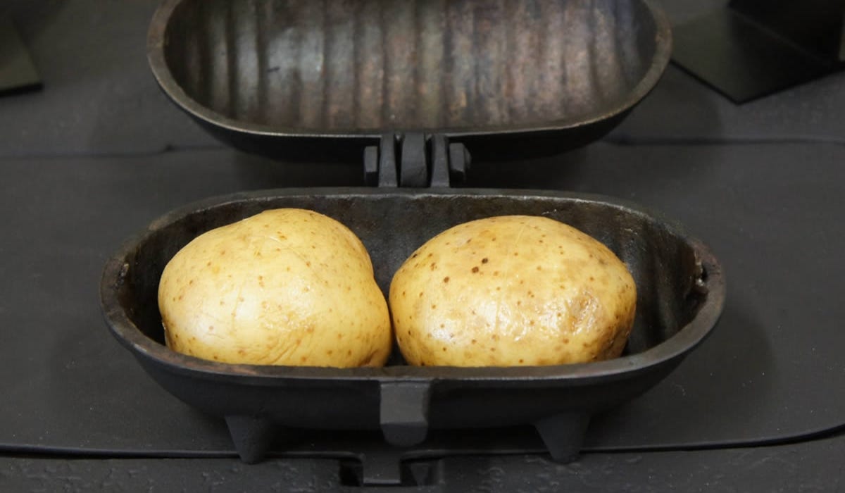 Two jacket potatoes inside a cast iron baked potato cooker