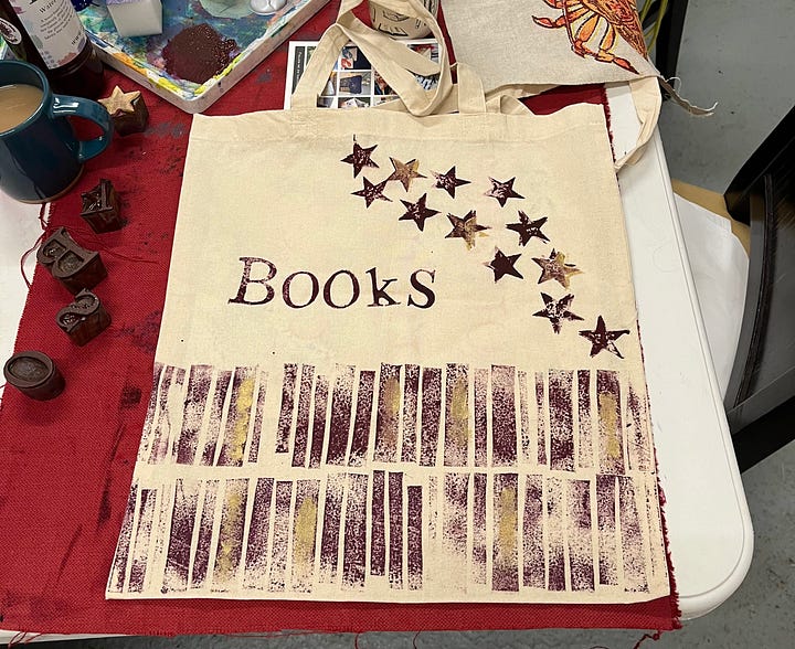 Hand-printed textiles; a tote bag with vaguely book-spine-ish pattern, the word 'BOOKS', and scattered stars; and a tea-towel with scattered green ferns and gold leaves, with one star in the melee.