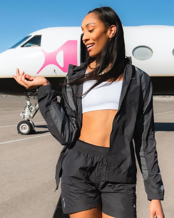 This may contain: a woman standing in front of an airplane with her hand on her hip and looking off to the side This may contain: a woman standing in front of an airplane with her hand on her hip and looking off to the side