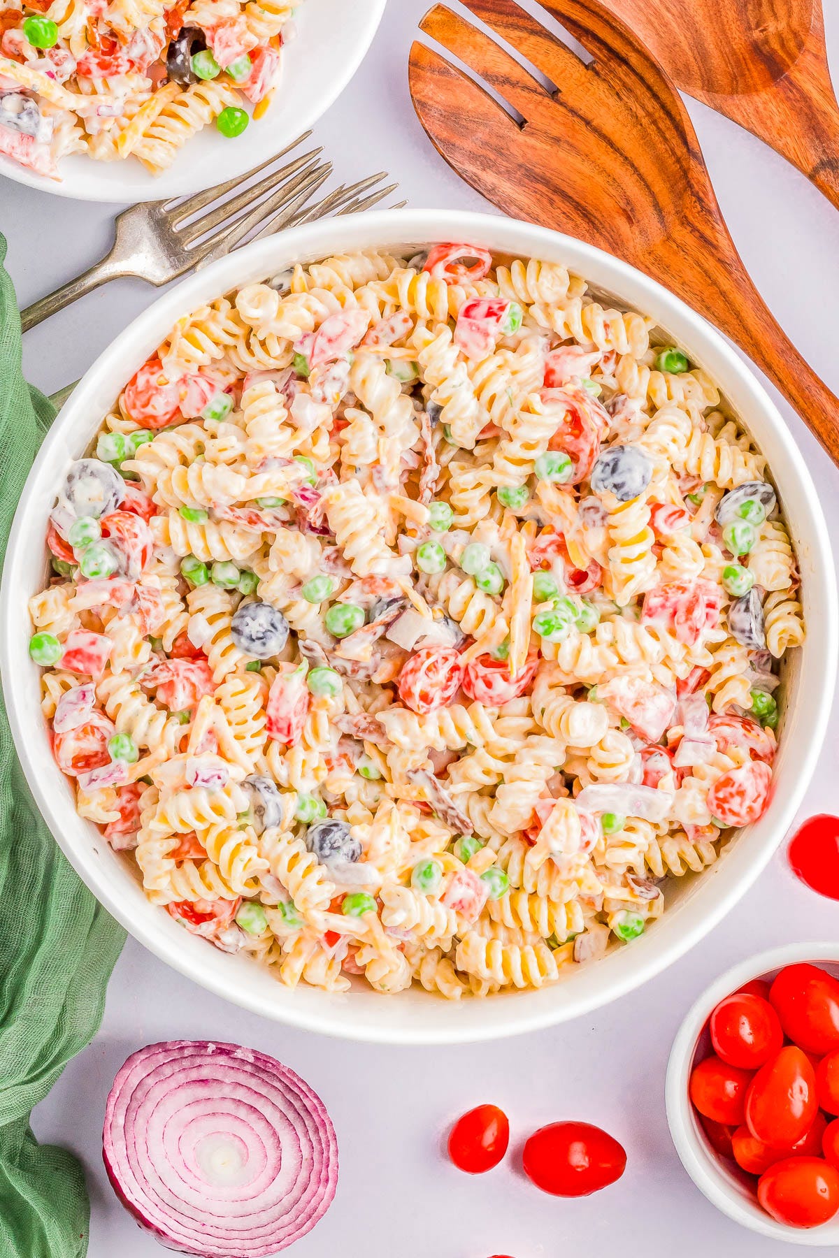 A bowl of rotini pasta salad with vegetables including peas, tomatoes, black olives, and diced red onions in a creamy dressing. 