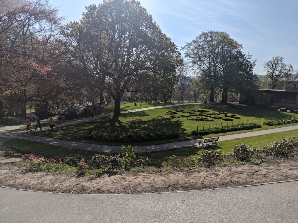 A lawn decorated by very low-pruned bushes is shaded by trees, with paths all around.