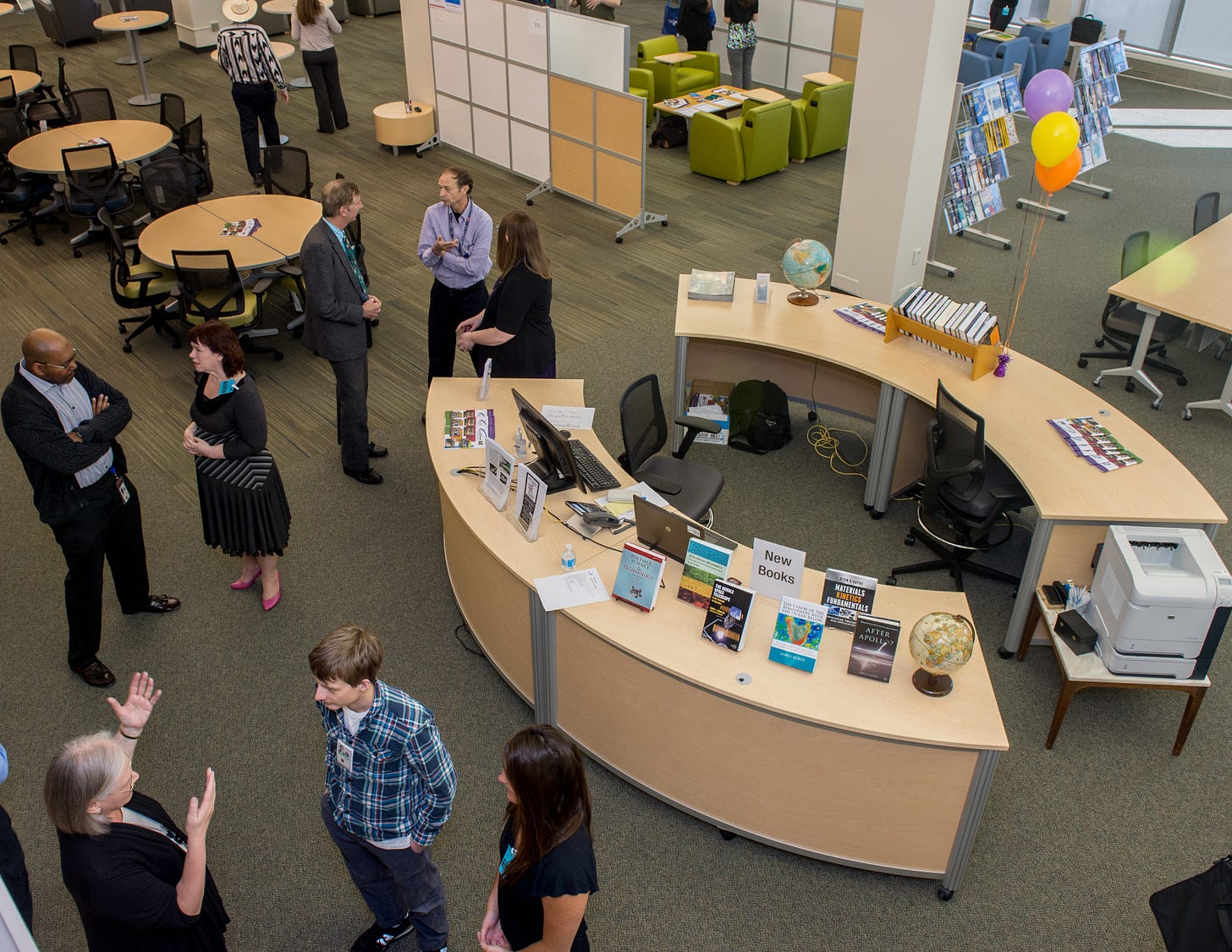 Ten people standing around a room, talking with one another, at the Grand Opening of the new Goddard Information and Collaboration Center in March 2016, with a full information desk, with books on display, and some balloons shown. Ten people standing around a room, talking with one another, at the Grand Opening of the new Goddard Information and Collaboration Center in March 2016, with a full information desk, with books on display, and some balloons shown.