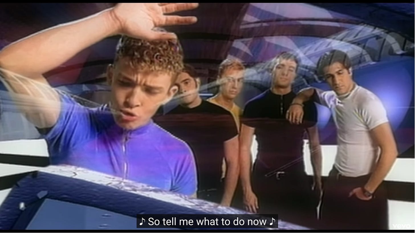 Justin is leaning against glass facing the camera and the other guys are leaning on each other looking forlorn while weird metallic looking shapes feature in the background and also partially obscure them Justin is leaning against glass facing the camera and the other guys are leaning on each other looking forlorn while weird metallic looking shapes feature in the background and also partially obscure them