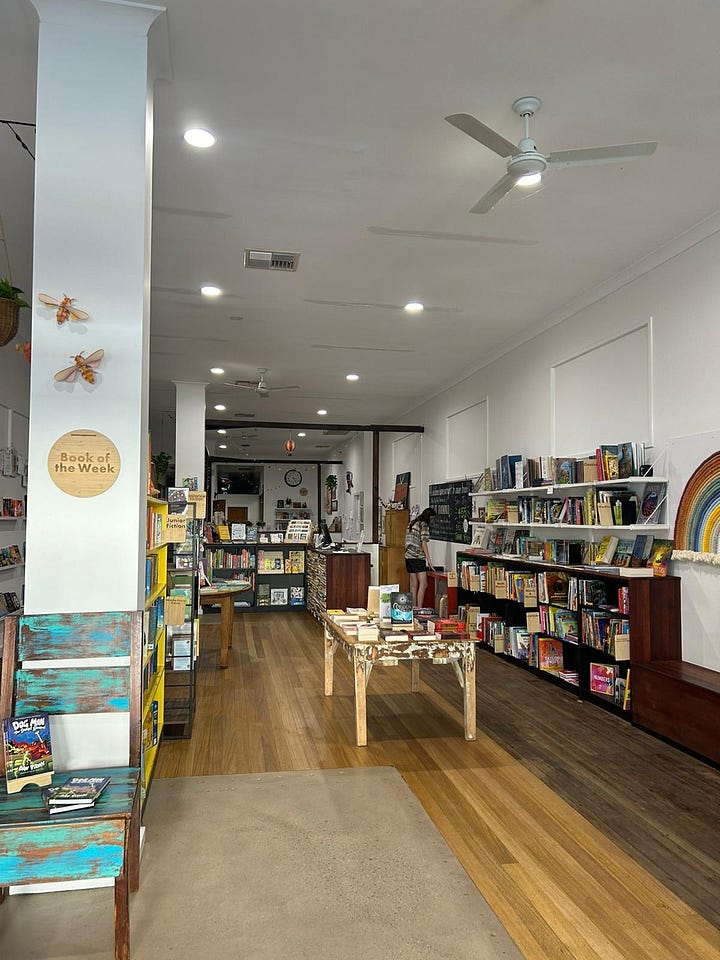 Photos of Bookshops. 1) The window display of Under the Silver Tree Cooperative Bookshop with trolleys of books ready to sell out the front. 2) The outside of The Broken Hill Bookshop - the front of the shop is painted white with a large sign displaying the store's name, the door is open to welcome customers inside. 3) A piece of craft paper on display inside Big Sky Stories divided into two sections. The first says "Is..." and the second says "Needs..." customers have written underneath the headings. 3) A photo of the inside of Big Sky Stories, there are lots of books on display, the inside is bright and welcoming.