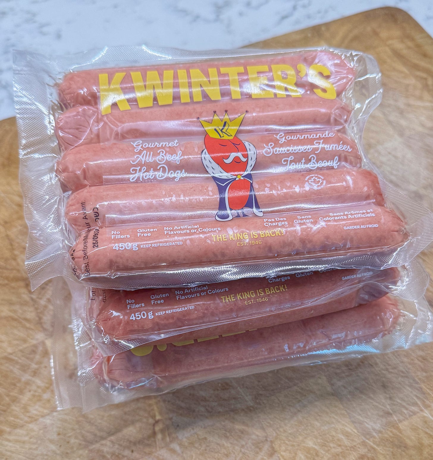 Four packages of Kwinters hot dogs (5 in each pack) stacked on a cutting board on a kitchen counter. 