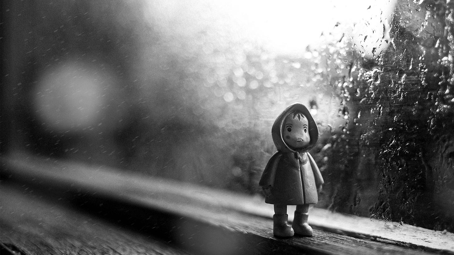 Small doll stands sadly on the window sill as it pours against the glass