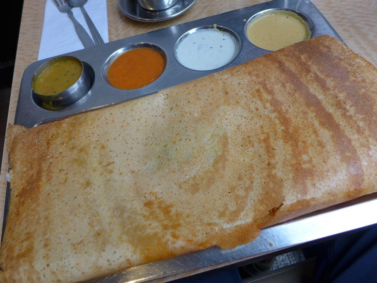 A rectangular dosa covers the metal tray, with found indentations for sauces.