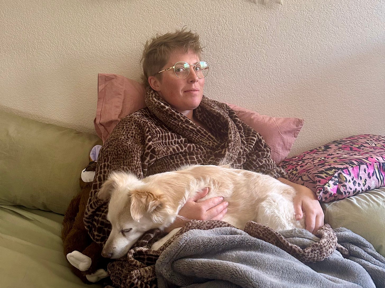 Xander in bed, wrapped in their robe with Lunie, their dog