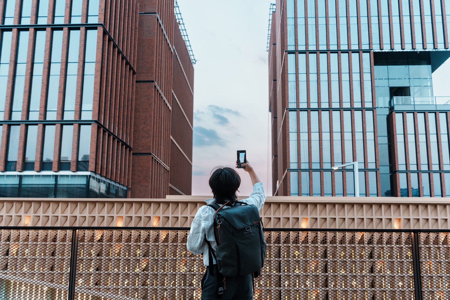 Person wearing a backpack standing in front of impressive urban buildings taking a photograph. Person wearing a backpack standing in front of impressive urban buildings taking a photograph.