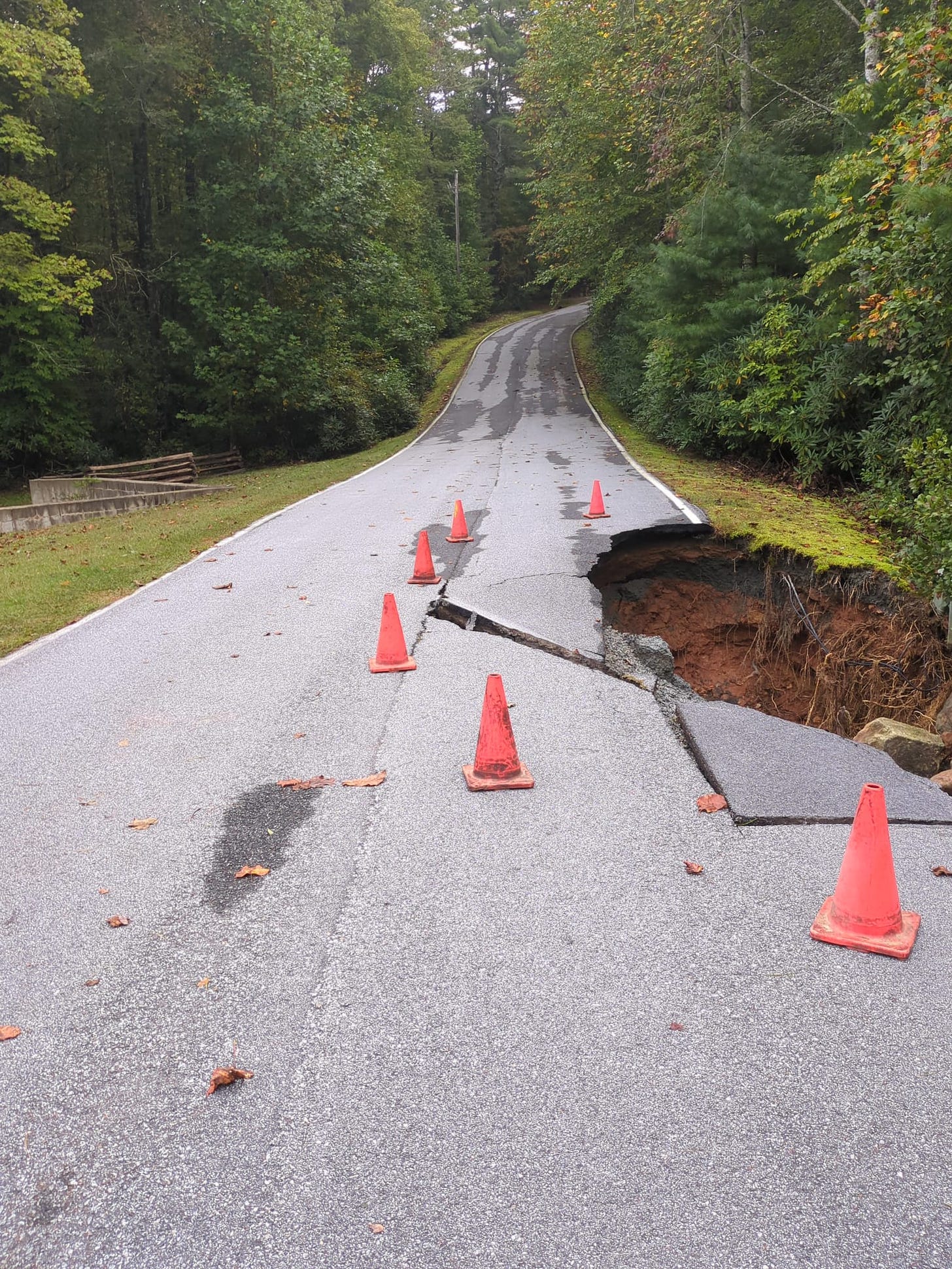 a broken road with orange safety cones around the hole
