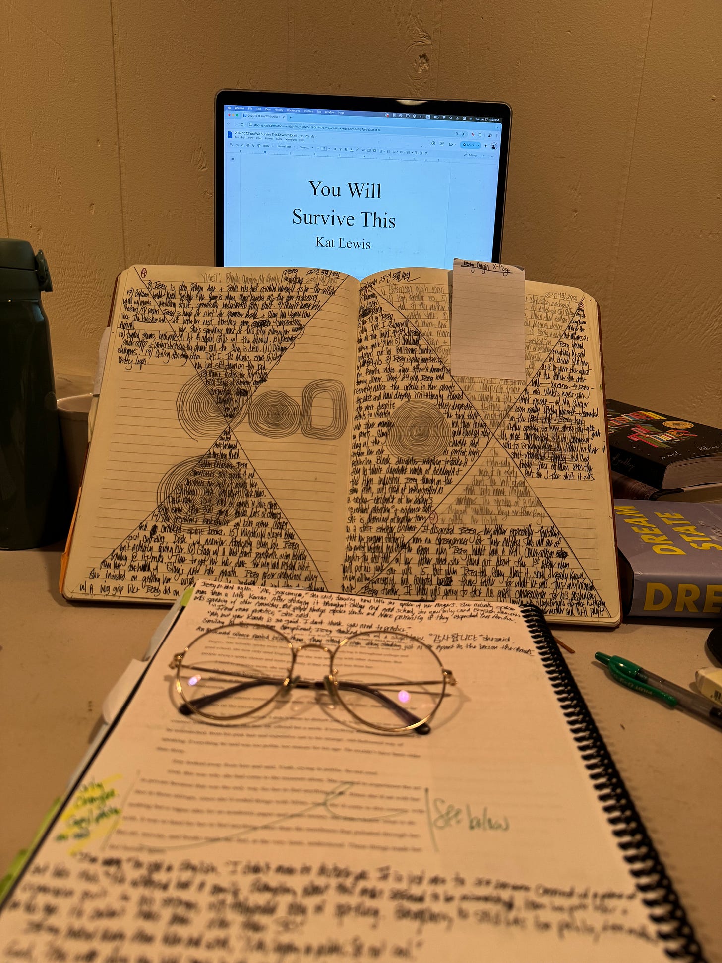 A photo of Kat’s laptop opened to the title page of her novel, You Will Survive This. Her notebook is opened to a Lynda Barry X Page writing exercise, and her printed manuscript is opened to a page filled with line notes. A photo of Kat’s laptop opened to the title page of her novel, You Will Survive This. Her notebook is opened to a Lynda Barry X Page writing exercise, and her printed manuscript is opened to a page filled with line notes.