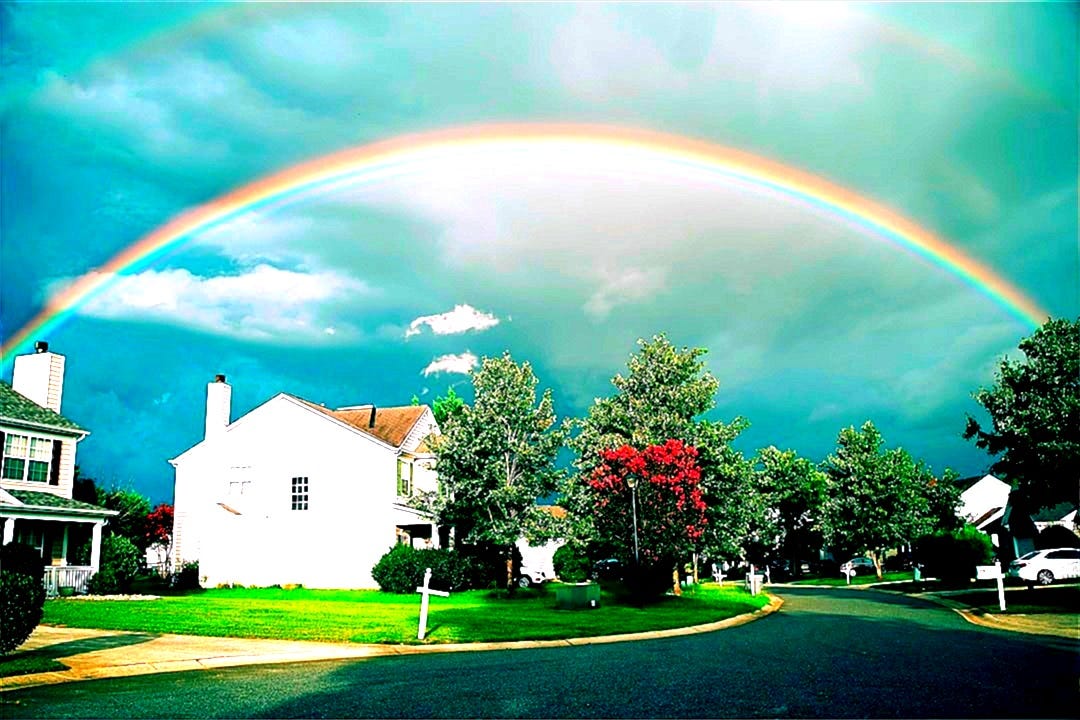 white concrete house near green trees under rainbow
