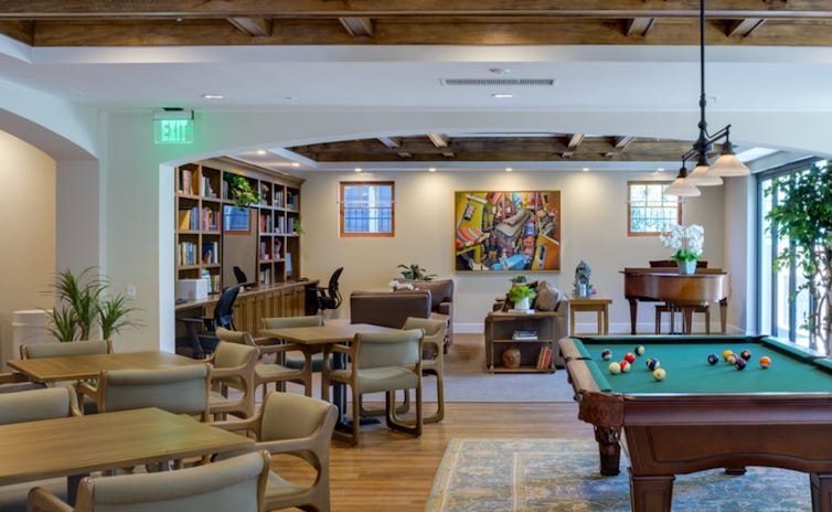 A spacious living space featuring a billiards table, chairs, tables and a large, built-in bookcase filled with books.