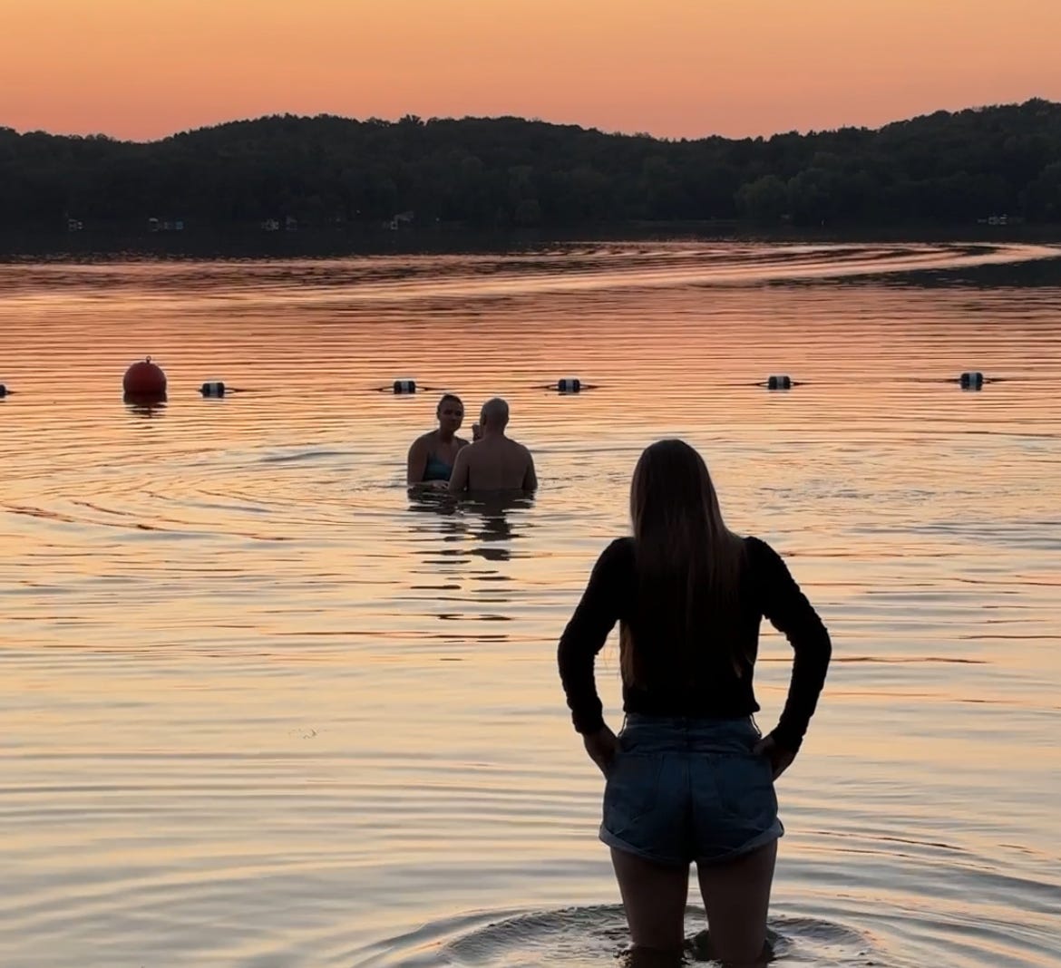 Picture shows shadows of individuals wading in the water as the sun sets. 
