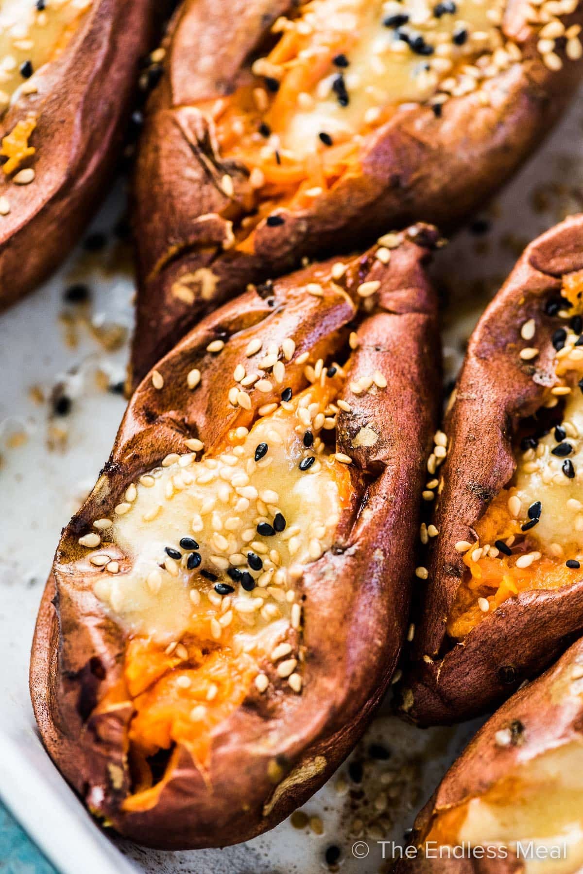 A close up of a roasted sweet potato cut open with miso tahini butter on top and a sprinkle of sesame seeds. A close up of a roasted sweet potato cut open with miso tahini butter on top and a sprinkle of sesame seeds.
