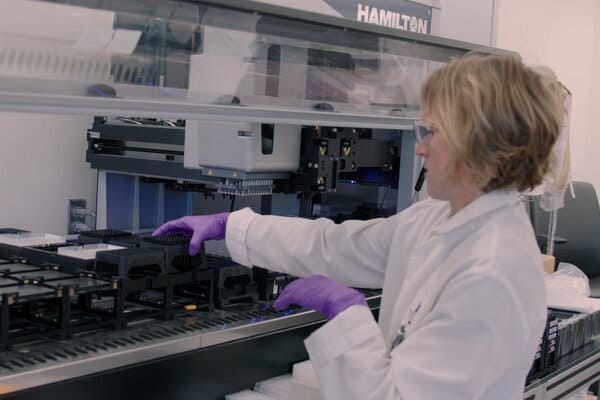 A lab technician places a plastic tray into a large complex machine in a lab.