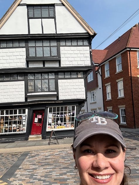 White woman poses awkwardly in front of cathedral and gardens