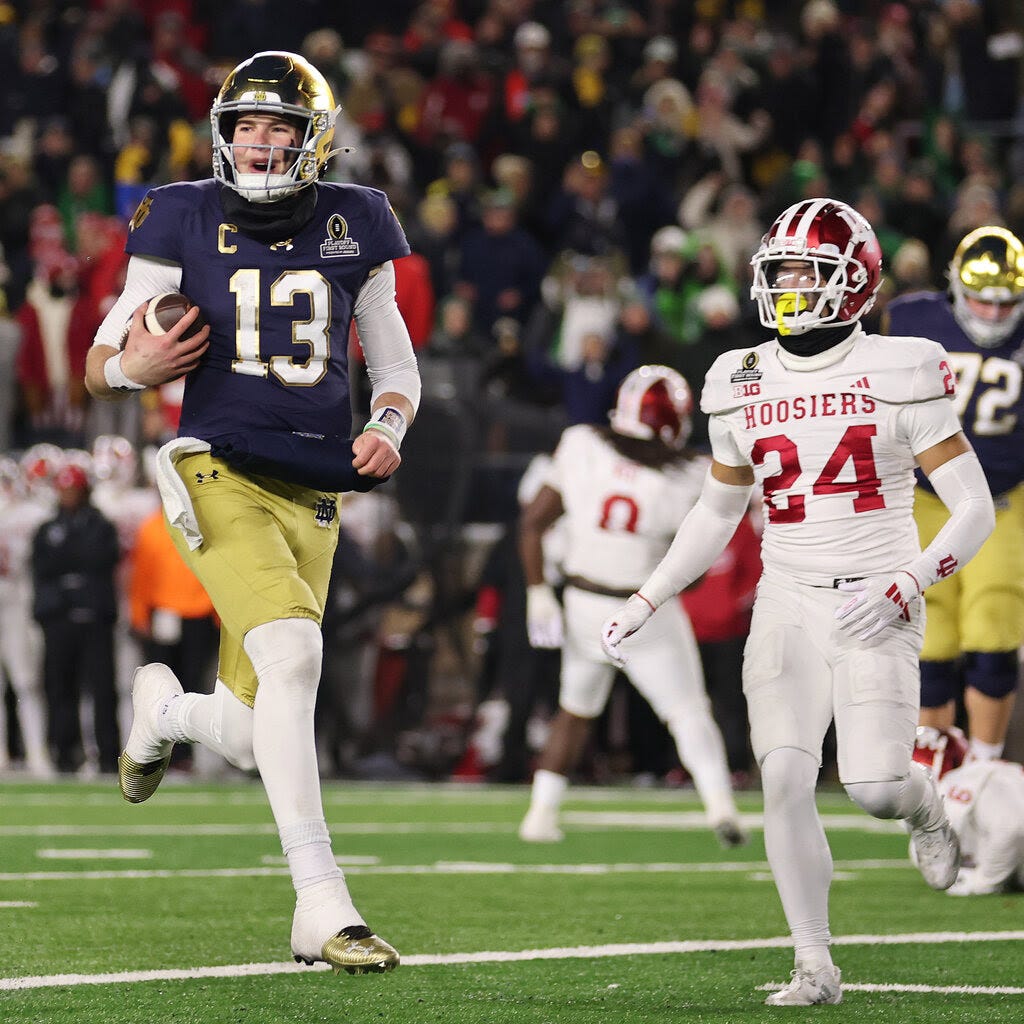 Notre Dame’s quarterback, in a blue jersey and gold pants, runs with the ball.