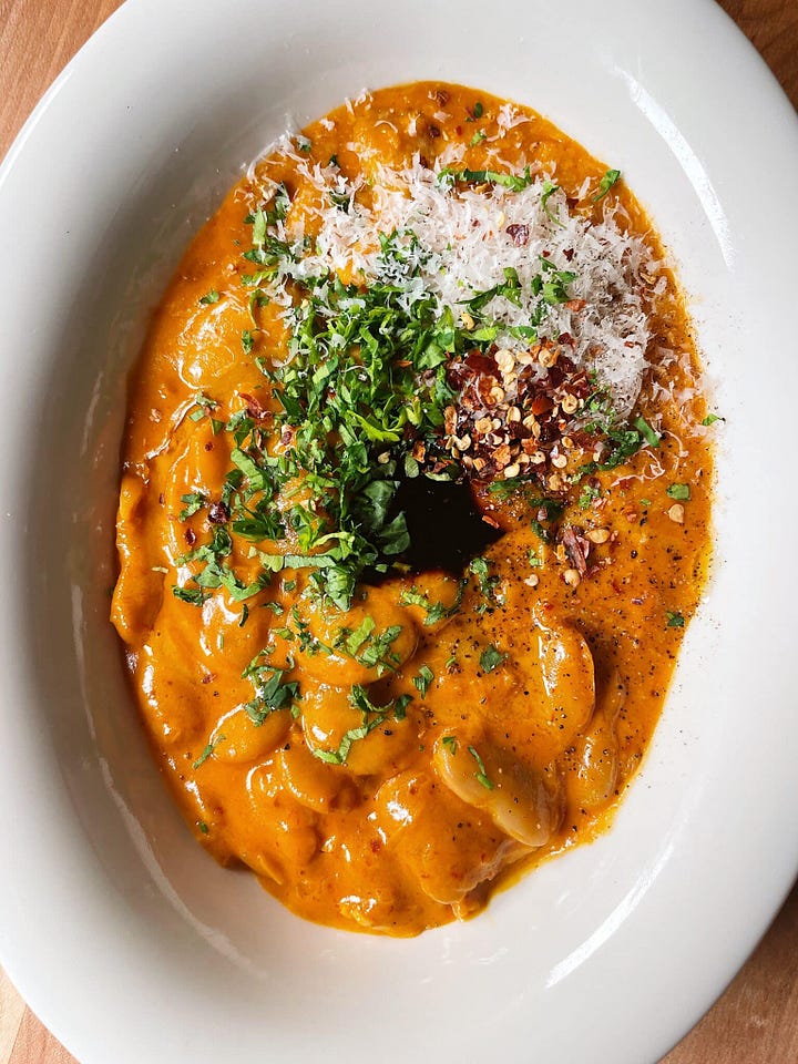 Left: A bowl of creamy beans in vodka sauce. Right: a small pink ceramic salt cellar.