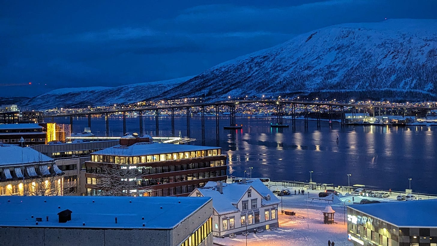 Tromso at night, twinkling in the deep blue light, the bridge stretching over the water, lights glimmering.