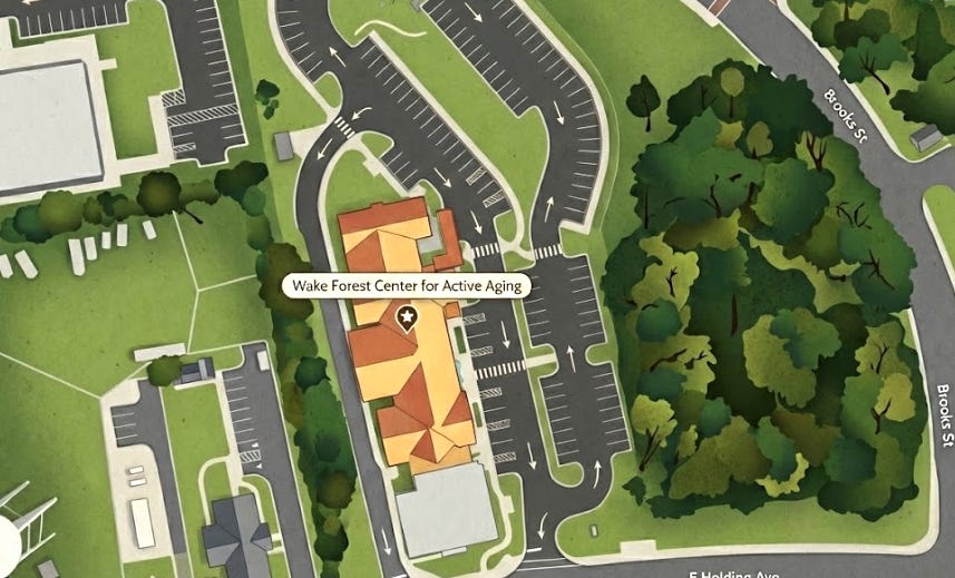 The image shows the main center building with an orange roof highlighted by a label and star icon, surrounded by extensive parking lots with directional arrows, green spaces, and a dense wooded area to the east. Streets named E Holding Ave and Brooks St border the site.