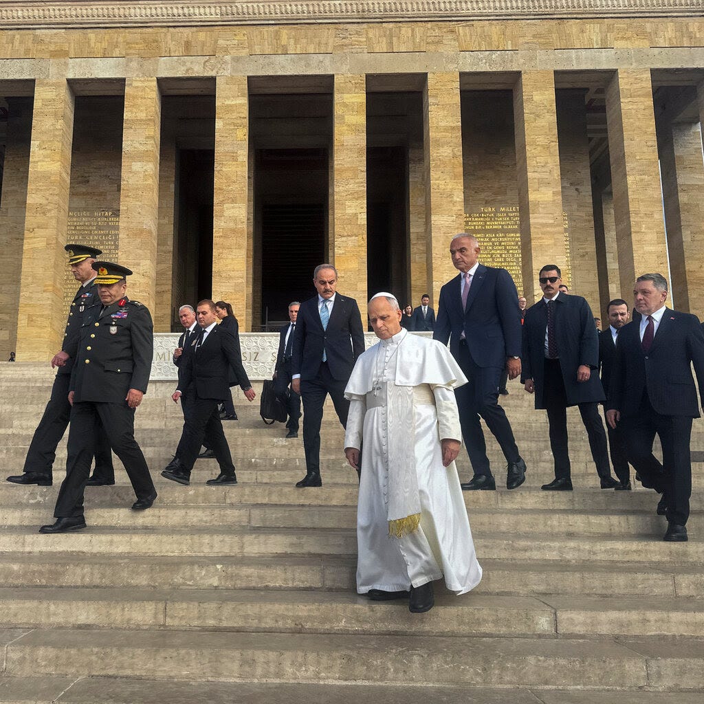 Pope Leo walks down stairs surrounded by officials. 