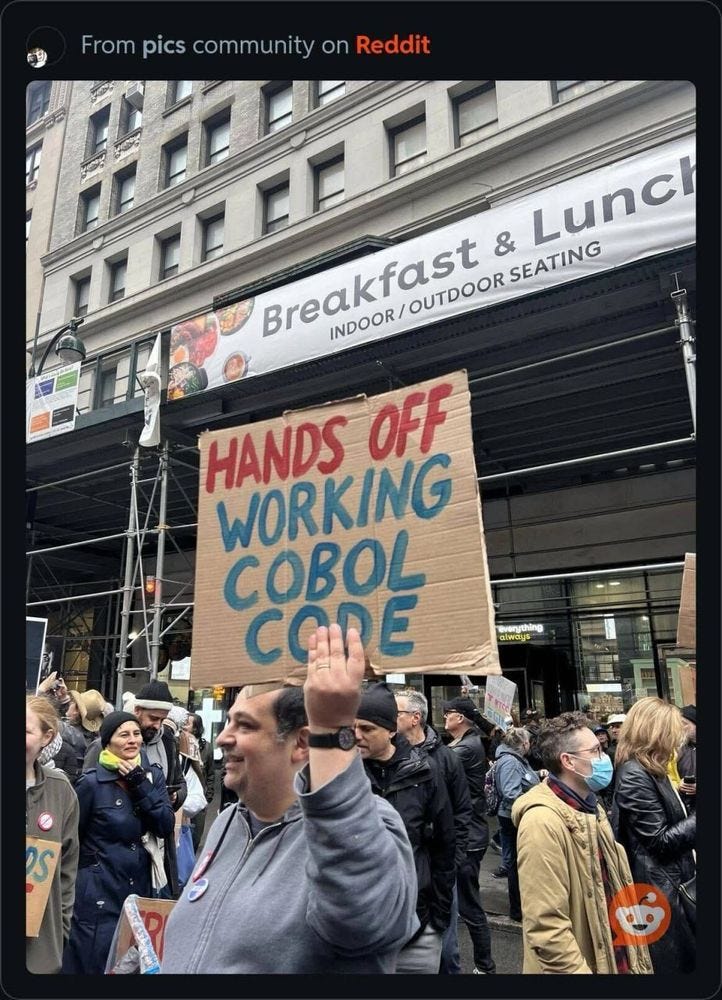 A guy carrying a protest sign that says "HANDS OFF WORKING COBOL CODE."