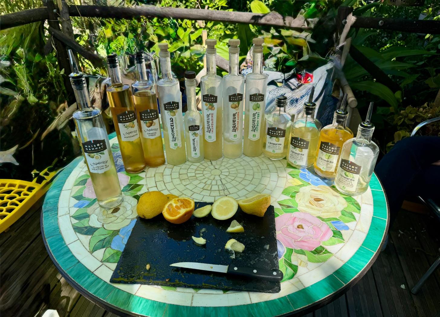 A tasting table with Maison Gannac limoncello, liqueurs, and aperitifs alongside freshly cut Menton lemons on a slate board.