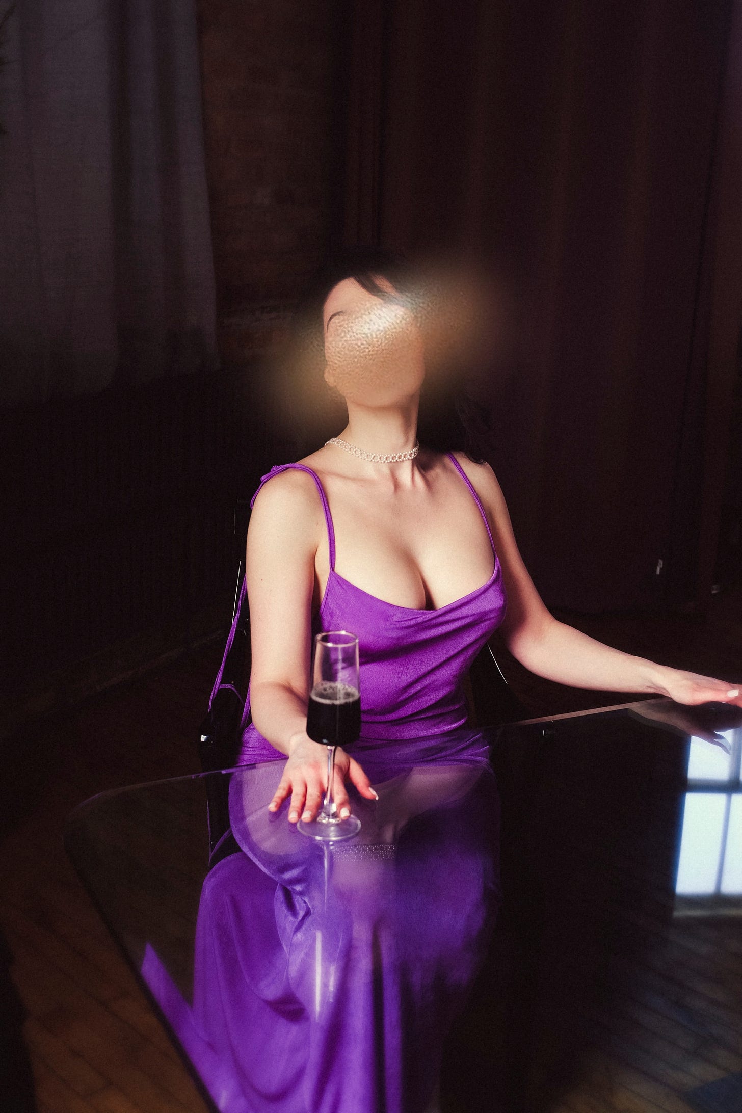 Elena is at a glass dining room table, a wall of red-toned brown curtains and brick behind her. She's wearing a gorgeous, low-backed purple goddess dress with thin, long spaghetti straps. She has on a lariat of small pearls in hexagon shapes curved around her neck like a choker. The dress is low on her chest, the fabric pulled just above her nipples and not a stitch more. Both of her hands are on the glass table, one holding the angular champagne flute with the dark foamy mystery liquid in it. Her dark hair is down and wavy, and she's looking off-camera.