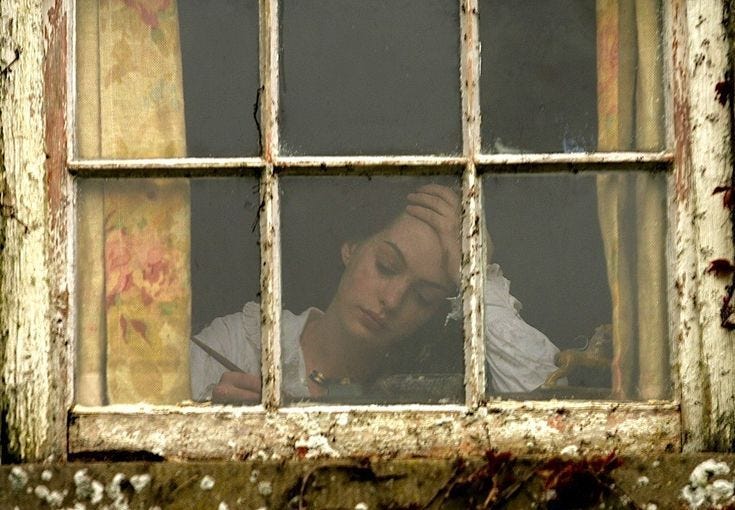 This may contain: a woman sitting in front of a window with her hand on her head and writing