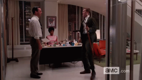 three men are standing in a room with a sign that says ' a.m.c.com '