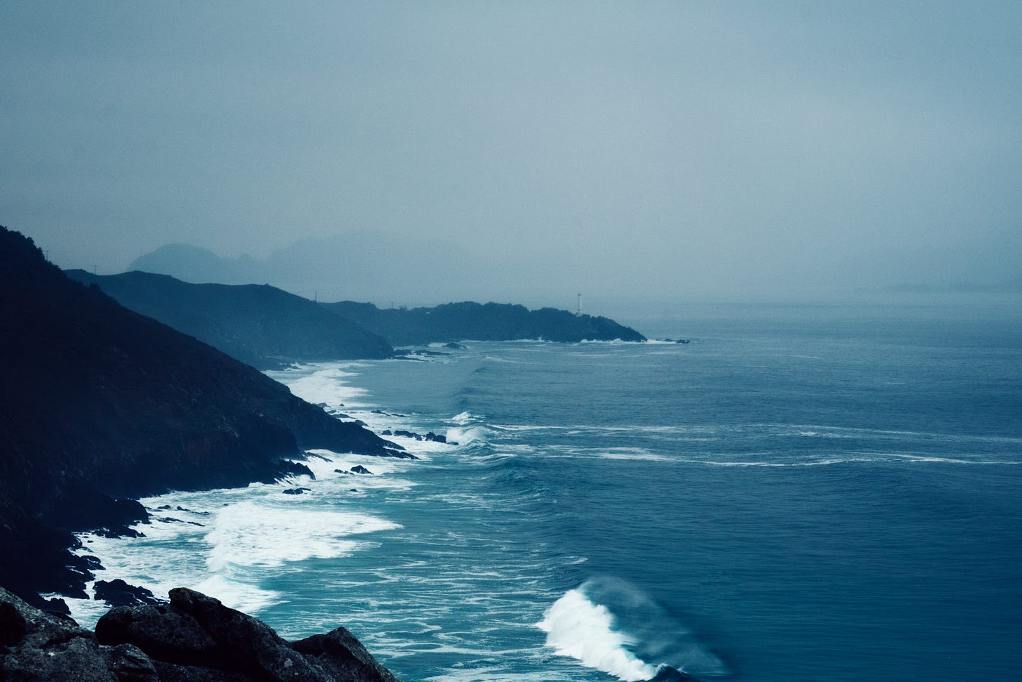 Waves crashing against rocky coastline against an overcast sky