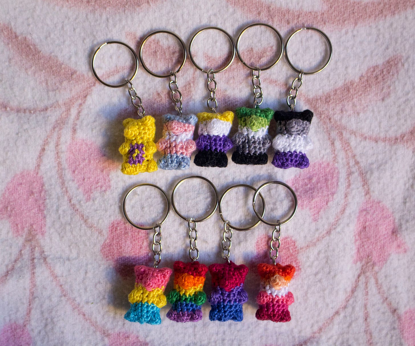 Nine small crocheted gummy bear keychains, each striped to look like different pride flags