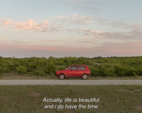 This may contain: a red car parked on the side of a road next to a lush green field
