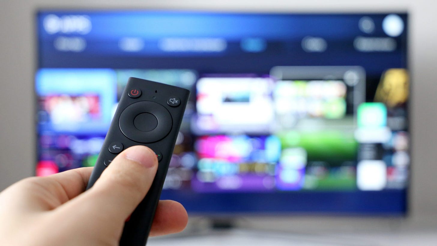 a hand holding a remote control with a smart tv in the background a hand holding a remote control with a smart tv in the background